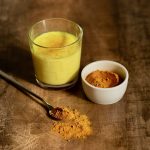 Golden Milk in a glass cup. Next to it is turmeric for making a drink and a spoon with spices. Dark background