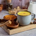 Traditional indian drink turmeric golden milk in a ceramic mug with ingredients